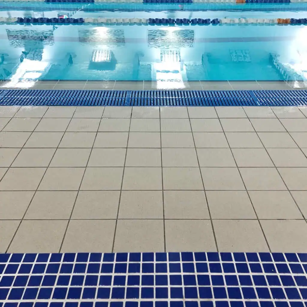 Indoor swimming pool with beige and blue tiled flooring for safety and aesthetics.